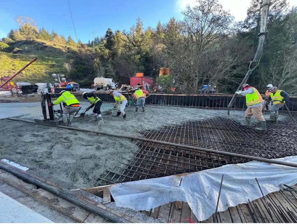 Workers pouring concrete over rebar on a bridge.