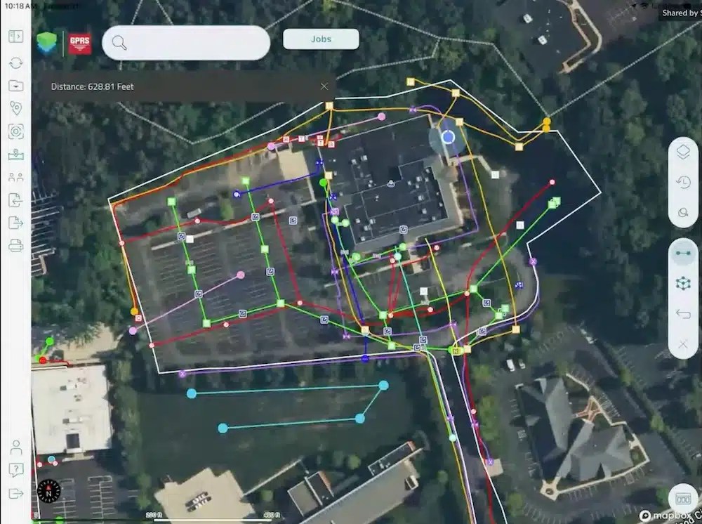 Aerial map view in the SiteMap mobile app showing a building and the surrounding area with color-coded utility lines and icons. The right toolbar includes options for layers, measurement tools, and settings, enabling users to manage base maps, imported layers, and utility data.