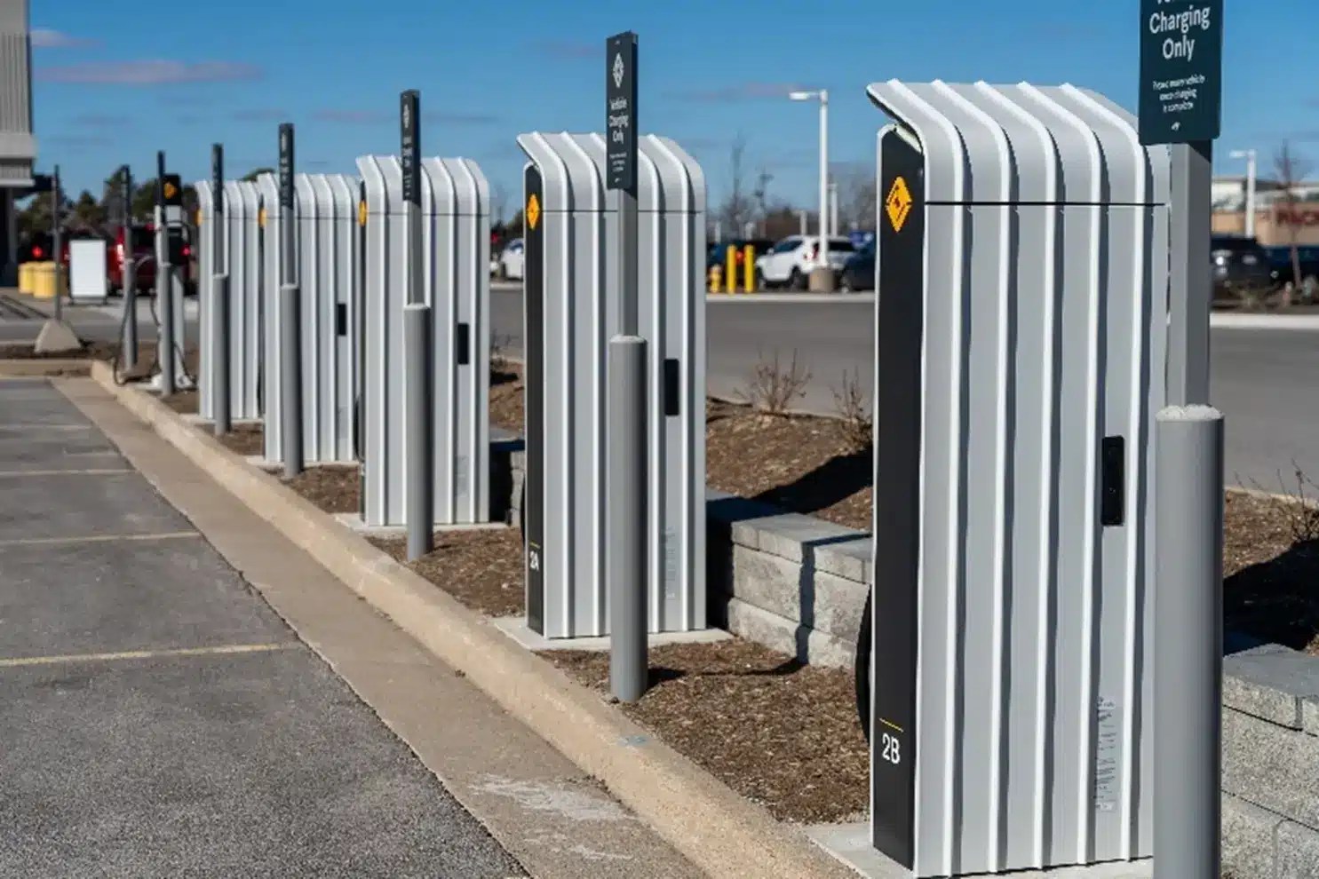 Row of modern electric vehicle charging stations lined up along a curb in a parking lot on a clear day.